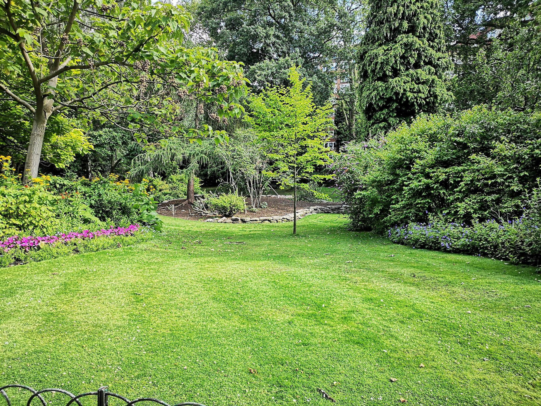 A manicured lawn edged with layered plantings and mature trees on a New England property